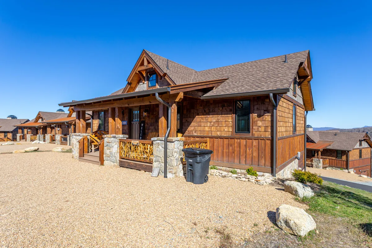 The exterior of The Roper Retreat, showcasing its welcoming wooden architecture and stone features set against a mountainous backdrop. A gravel pathway leads up to the home, inviting guests to explore the natural surroundings.
