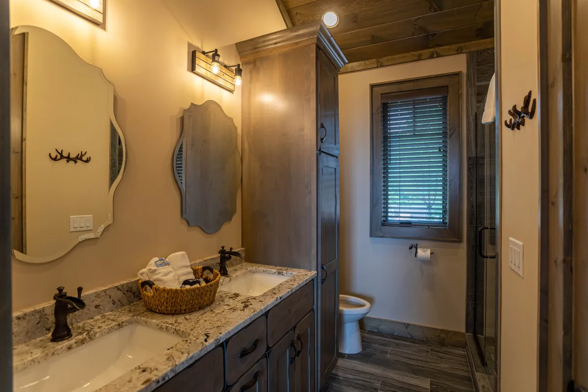 A luxurious ensuite bathroom with double granite sink vanity, sleek wooden cabinetry, decorative mirrors, and a glimpse of a tiled shower area, creating a spa-like environment.