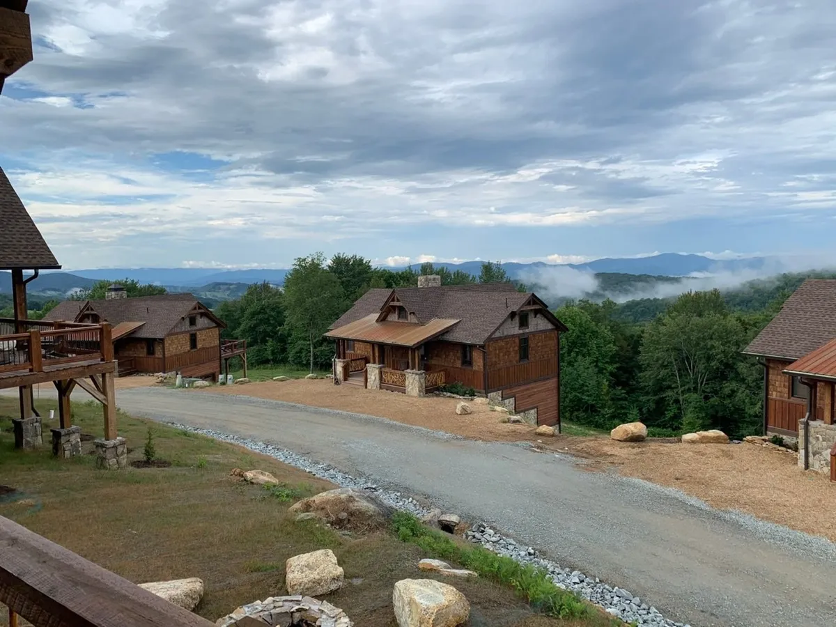 This image depicts a group of wooden cabins nestled against a scenic mountain backdrop. A gravel pathway winds through the property, inviting exploration and family walks. The setting feels serene and naturally beautiful, ideal for outdoor enjoyment.