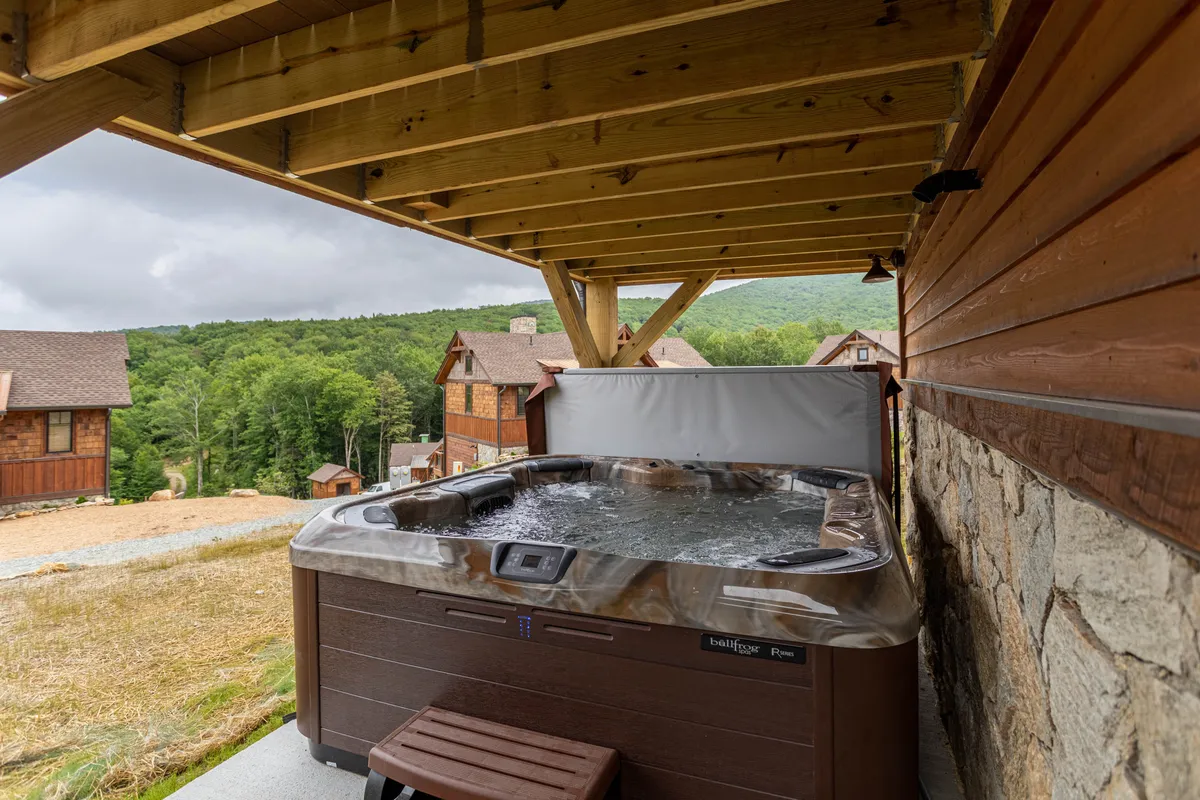 A steaming hot tub sits beneath wooden beams with sweeping views of the surrounding mountains. The space looks tranquil and inviting, ideal for unwinding after a day of adventures.